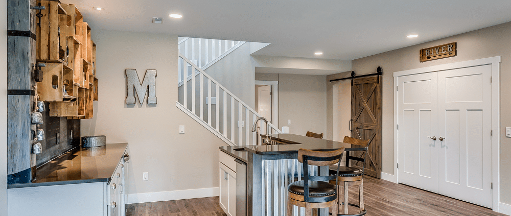 A modern kitchen featuring a bar area and staircase, showcasing LVP flooring in a stylish basement remodel.