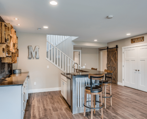 A modern kitchen featuring a bar area and staircase, showcasing LVP flooring in a stylish basement remodel.