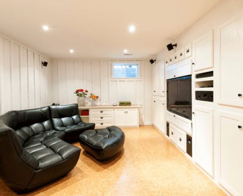 A room featuring a black leather couch and a television, designed for family entertainment in a remodeled basement.